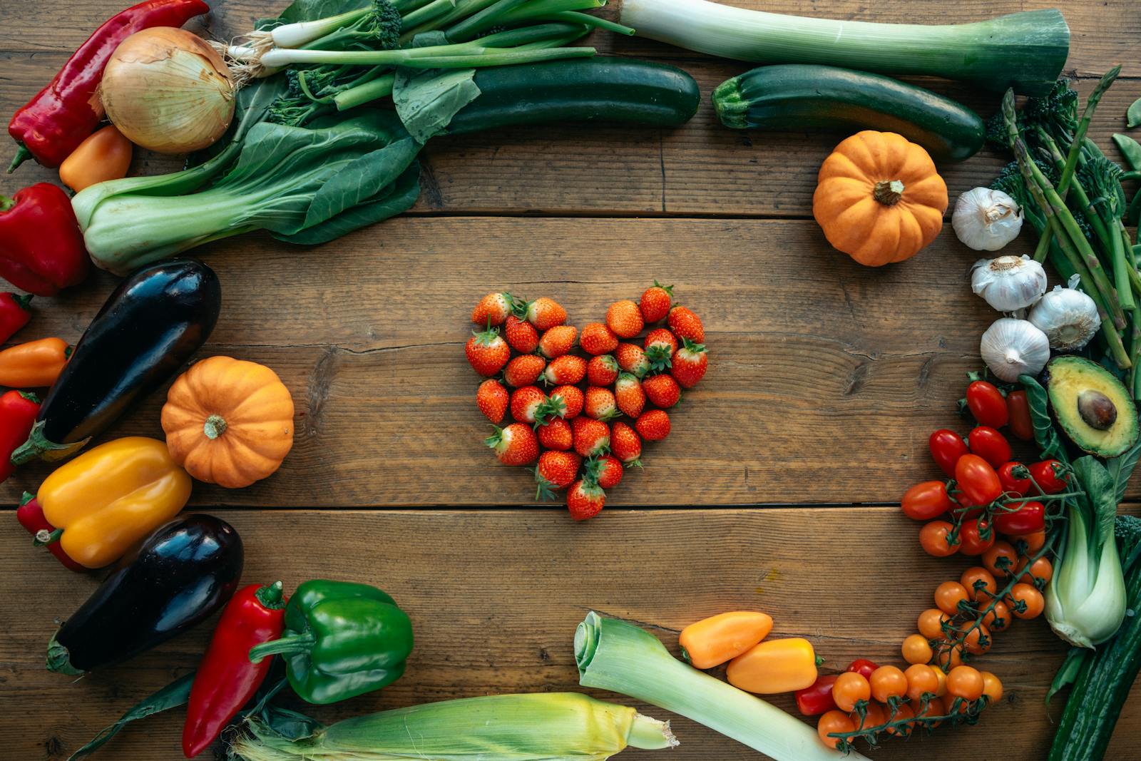 Vibrant fruits and vegetables arranged heart-shaped on a wooden surface, top view.